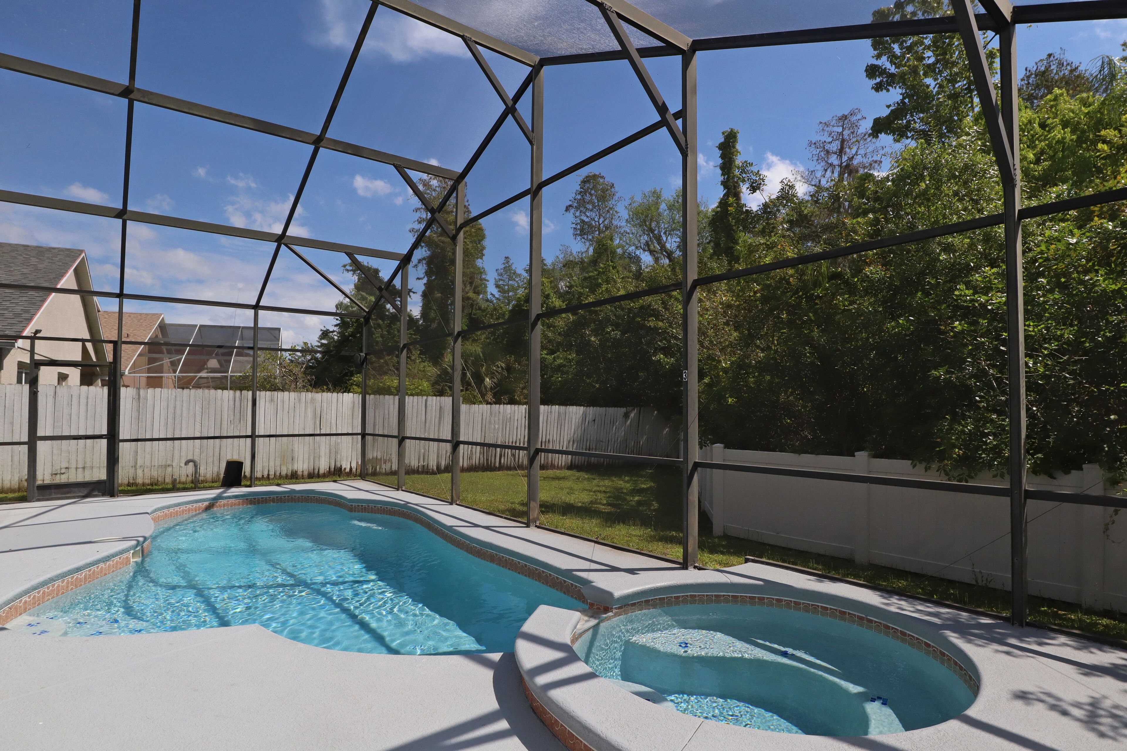 Un patio trasero con piscina, cerca de madera y cielo despejado.