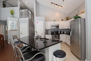 A modern kitchen with a central island, stainless steel appliances, and a staircase leading to an upper level. - Diamond!  Super Spacious,Private Pool & Spa, 
 6 Bedroom Home (Kissimmee)