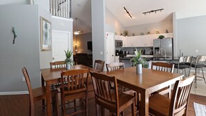Un vaste espace dédié à la salle à manger, avec une table et des chaises en bois, une cuisine à l’arrière-plan et un escalier menant à l’étage supérieur.