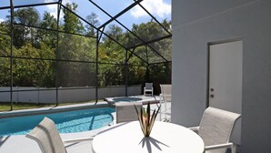 Un espace aménagé au bord de la piscine, avec une terrasse couverte, une table ronde et deux chaises.