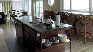Una cocina amplia con una isla grande, luces colgantes y vistas al exterior a través de amplios ventanales.