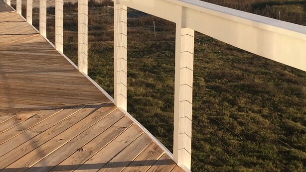Una terraza de madera con barandillas blancas que da a una playa y el océano.