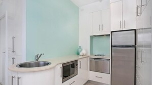 Een moderne keuken met witte kastjes, een roestvrijstalen spoelbak, een inbouwoven, een vaatwasser en een koelkast met dubbele deuren.