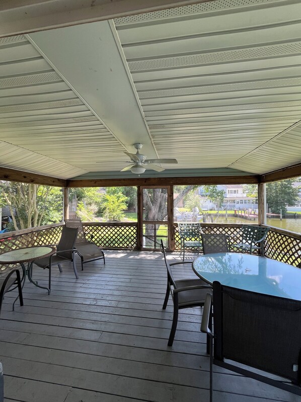 A covered patio with a table and chairs, a ceiling fan, and a view of a river and houses. - Spacious Home, With Dock, Sleeps 9, Access To Beach Club & Pool (Ocean Pines)