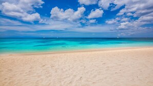 Une plage bordée d’une eau turquoise et limpide, avec un rivage sablonneux, sous un ciel bleu parsemé de quelques nuages.
