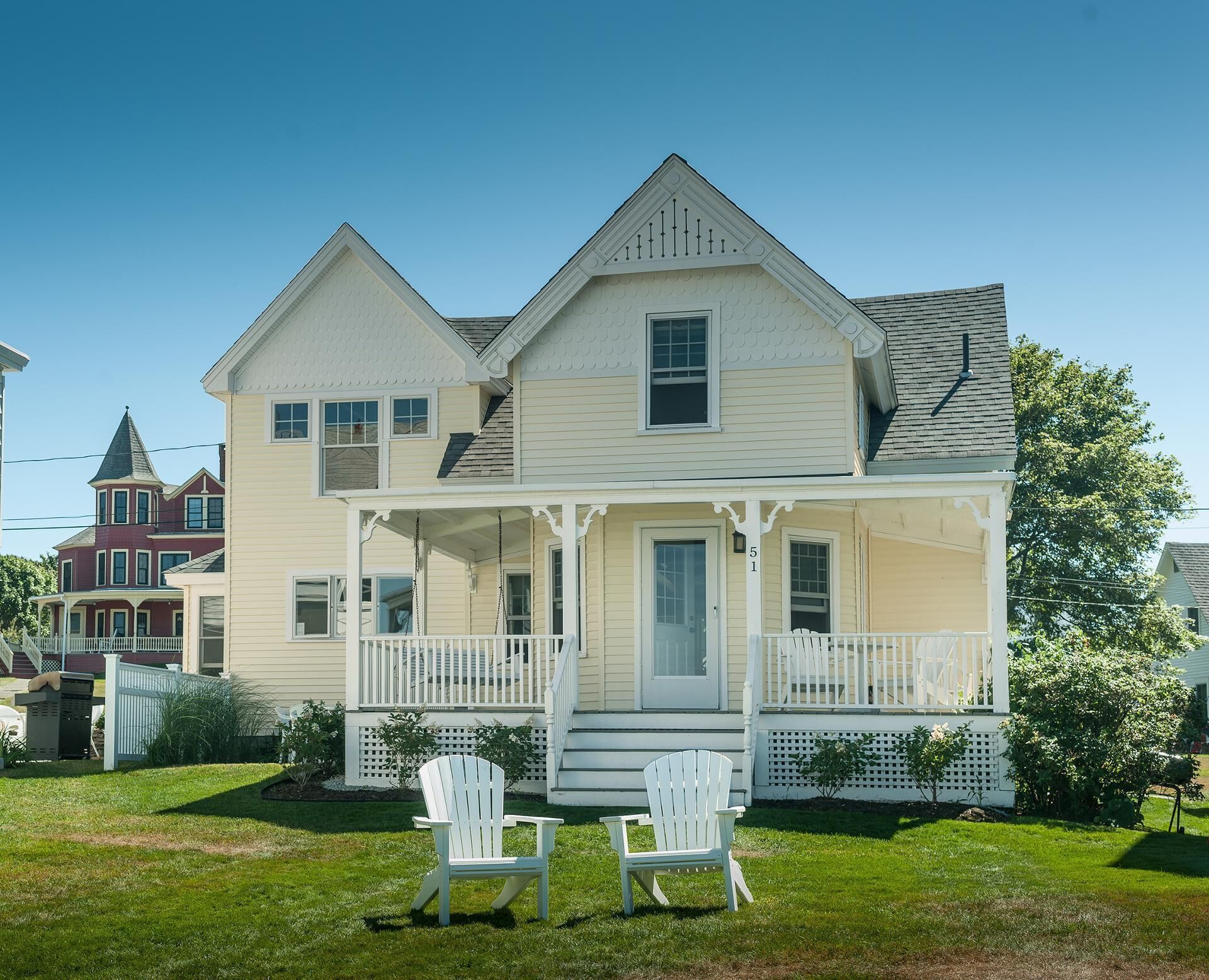 Ein zweistöckiges Haus mit Veranda und zwei Adirondack-Stühlen.