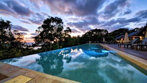 A swimming pool with a view of the ocean and trees at sunset. - TREE HOUSE - SUNRISE AT 1770 (AGNES WATER)