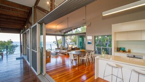 A modern interior with a wooden deck, a dining area, and a kitchen with a large window. - TREE HOUSE - SUNRISE AT 1770 (AGNES WATER)
