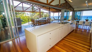 A modern kitchen with a large island, wooden flooring, and a view of the ocean. - TREE HOUSE - SUNRISE AT 1770 (AGNES WATER)