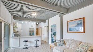 Uma cozinha moderna com ilha central, banquetas de bar e um espaço de estar com sofá e almofadas.