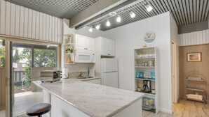 Uma cozinha moderna com armários brancos, bancada de granito e micro-ondas embutido. Há uma janela grande que oferece iluminação natural e vista para o exterior.