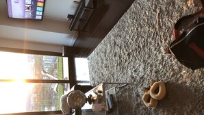 A living room with a large window, a flat-screen TV mounted on the wall, a leather sofa, a glass coffee table, and a fluffy rug. - Quiet 2/2 High-rise at the Tallahassee Center (Tallahassee)