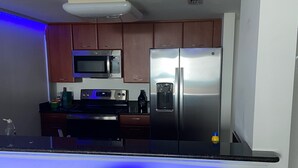A modern kitchen with stainless steel appliances, wooden cabinets, and a bar area with two stools. - Quiet 2/2 High-rise at the Tallahassee Center (Tallahassee)