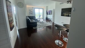 A spacious living area with a dark wood floor, a black leather sofa, and a glass coffee table. There is a large window providing a view of the outdoors. - Quiet 2/2 High-rise at the Tallahassee Center (Tallahassee)