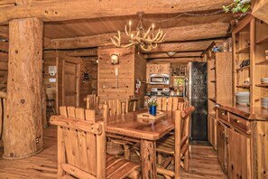 Un interior rústico de madera con una mesa de comedor, sillas, una araña y una zona de cocina.