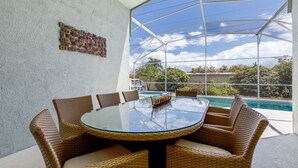 A glass-top table with wicker chairs in a sunlit room with a view of a swimming pool and greenery. - Beautiful villa in popular Indian Creek (Kissimmee)