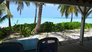 A beach view with a wooden deck, two chairs, and a table. - Beachfront large one bedroom studio, adjoining studio can be added to make 2/2. (Spanish Wells)