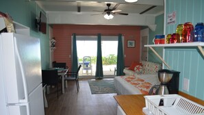 A compact room with a bed, a desk, a chair, a refrigerator, a coffee maker, and a shelf with colorful containers. - Beachfront large one bedroom studio, adjoining studio can be added to make 2/2. (Spanish Wells)