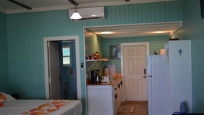 A compact room with teal walls, a bed with an orange fish-patterned bedspread, a kitchenette with a refrigerator, and a door leading to another room. - Beachfront large one bedroom studio, adjoining studio can be added to make 2/2. (Spanish Wells)
