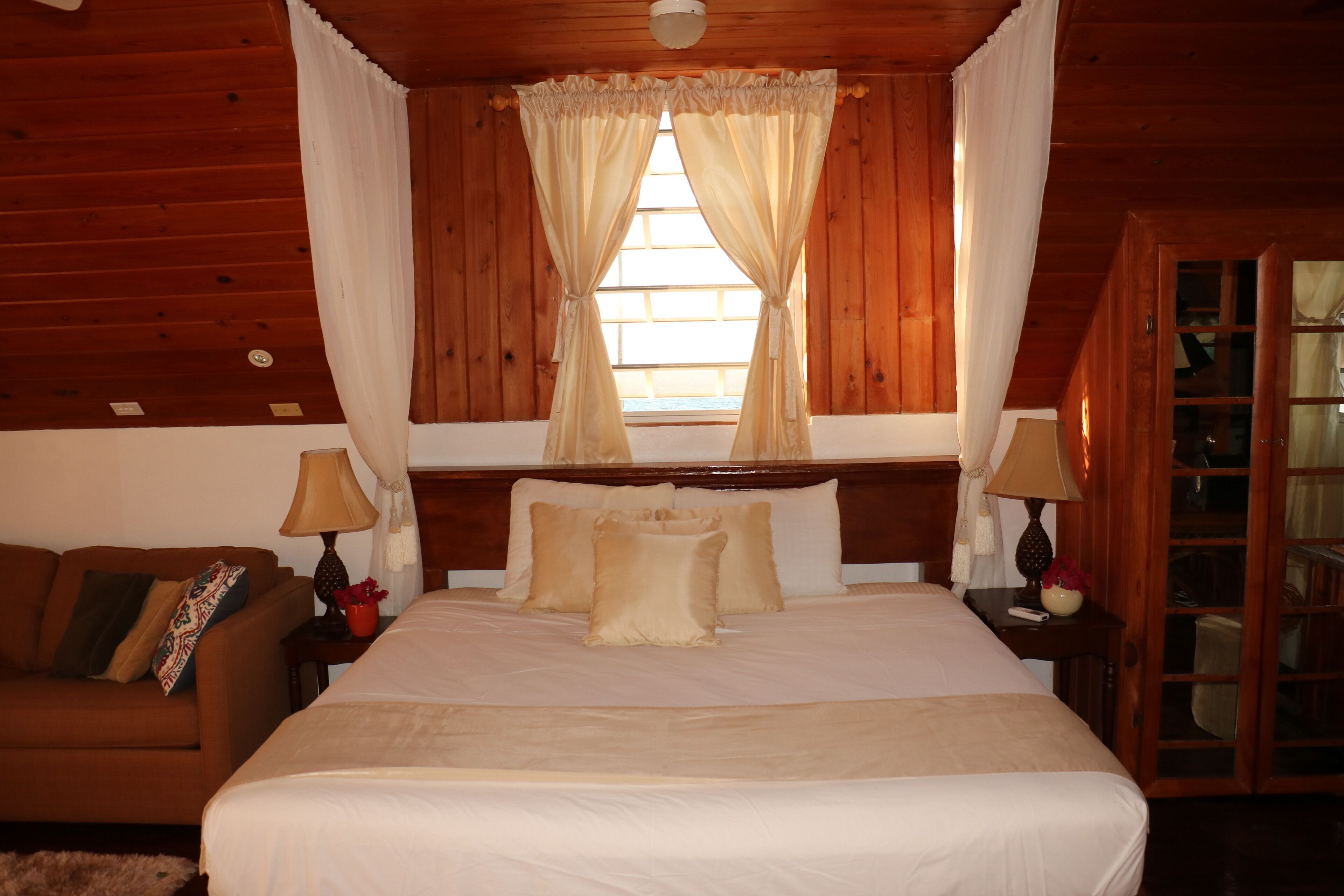 A cozy bedroom with a large bed, a wooden headboard, a nightstand with lamps, and a window with curtains.