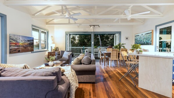 A spacious living area with a wooden floor, a sofa, a dining table with chairs, and a kitchen area with a counter and stools.