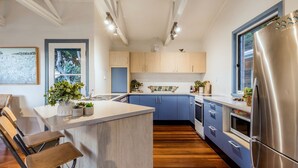 Una cocina moderna con una isla central, armarios de madera, un refrigerador de acero inoxidable y un ventanal que proporciona luz natural.