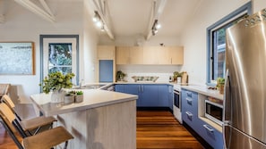 Una cucina moderna con isola centrale, mobili in legno, frigorifero in acciaio inossidabile e una finestra che offre luce naturale.