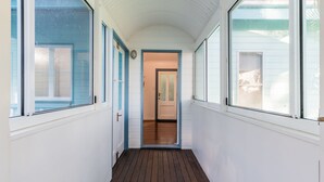 Un pasillo con paredes blancas, suelo de madera y ventanas grandes a ambos lados.