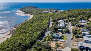Vista aerea di una zona residenziale costiera con case, una spiaggia e una collina boscosa.