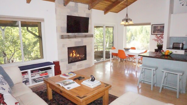 Uma sala de estar espaçosa com lareira, uma área de jantar com cadeiras laranja e uma cozinha com banquetas.