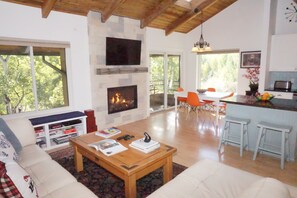 A spacious living area with a fireplace, a dining area with orange chairs, and a kitchen with bar stools. - Newly Remodeled Close to everything in Snowmass Village (203090-2371) (Snowmass Village)
