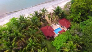 An aerial view of a resort with a swimming pool, red-roofed structures, and a beach.