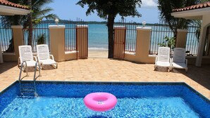 A swimming pool with a pink float ring, surrounded by lounge chairs and a view of the sea.