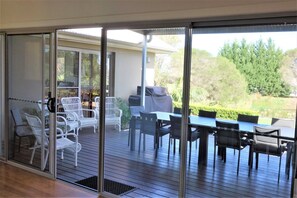 A covered patio with outdoor furniture, including chairs and tables, and a view of a garden and trees.