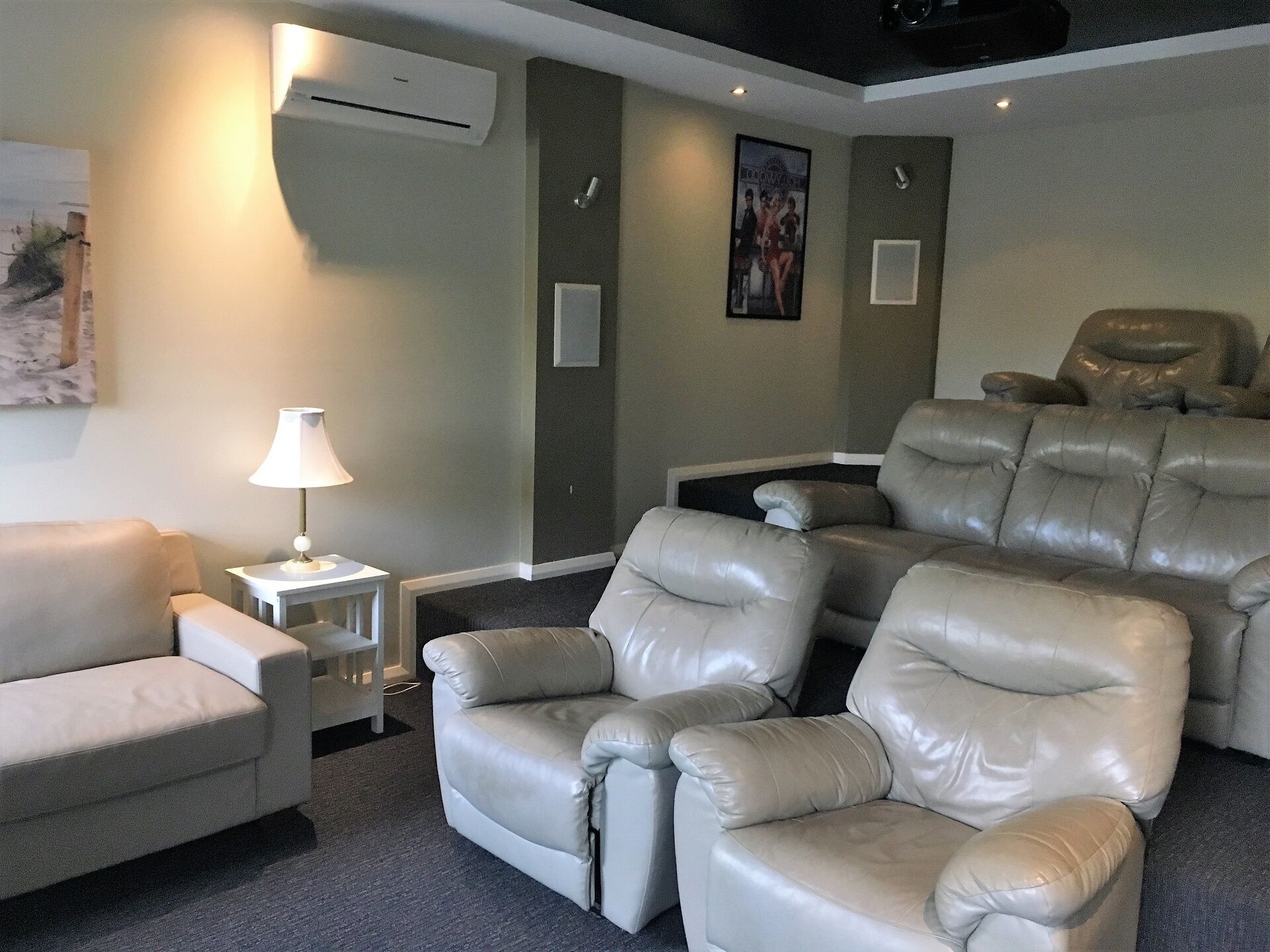 Une salle de cinéma maison équipée d’un fauteuil en cuir inclinable, d’un fauteuil blanc et d’une petite table avec une lampe.