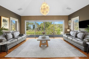 A modern living room with two grey sofas, a central coffee table, and a large window offering a view of greenery. - Stunning Mystique Country House with lake & mountain. 15% discount all winter. (Coolangatta)