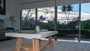 Un salón moderno con un ventanal grande, una mesa blanca y un jarrón con flores moradas.