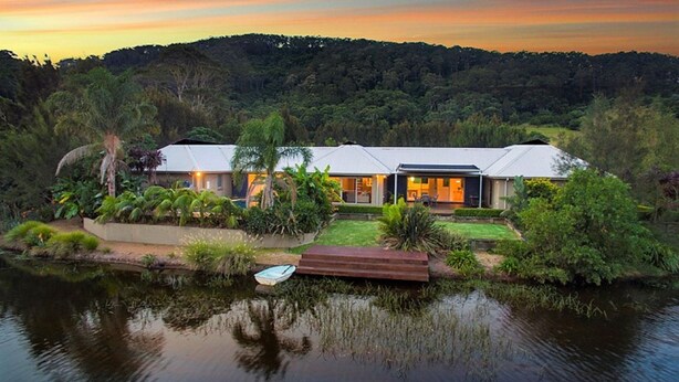 Una casa moderna con una amplia terraza con vistas a un lago, rodeada de exuberante vegetación.