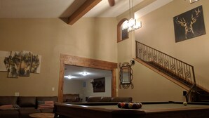 Uma sala de estar com mesa de bilhar, escada e lustre.