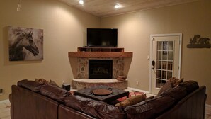 Sala de estar com lareira de pedra, sofá de couro e televisão na parede.