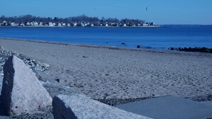 A beach with a rocky shoreline and a row of houses in the background.