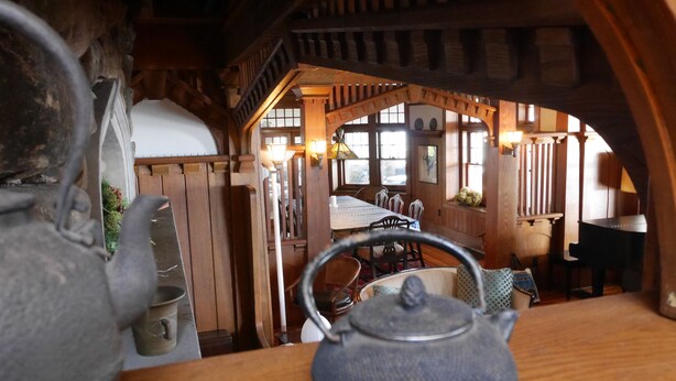 A rustic interior with a wooden table, a teapot, and a view of a dining area with chairs and a table.