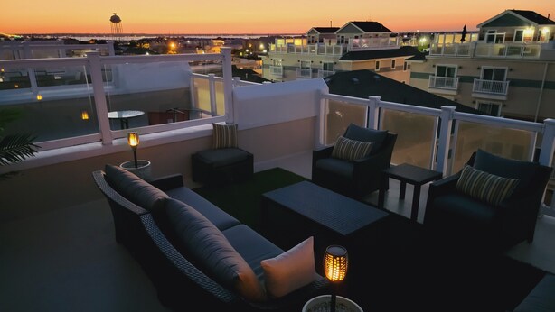 Terraza en la azotea con mobiliario exterior, una planta en maceta y vista panorámica del paisaje urbano al atardecer.