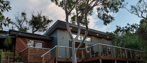 A modern two-story building with a wooden deck and a staircase leading to the upper level.