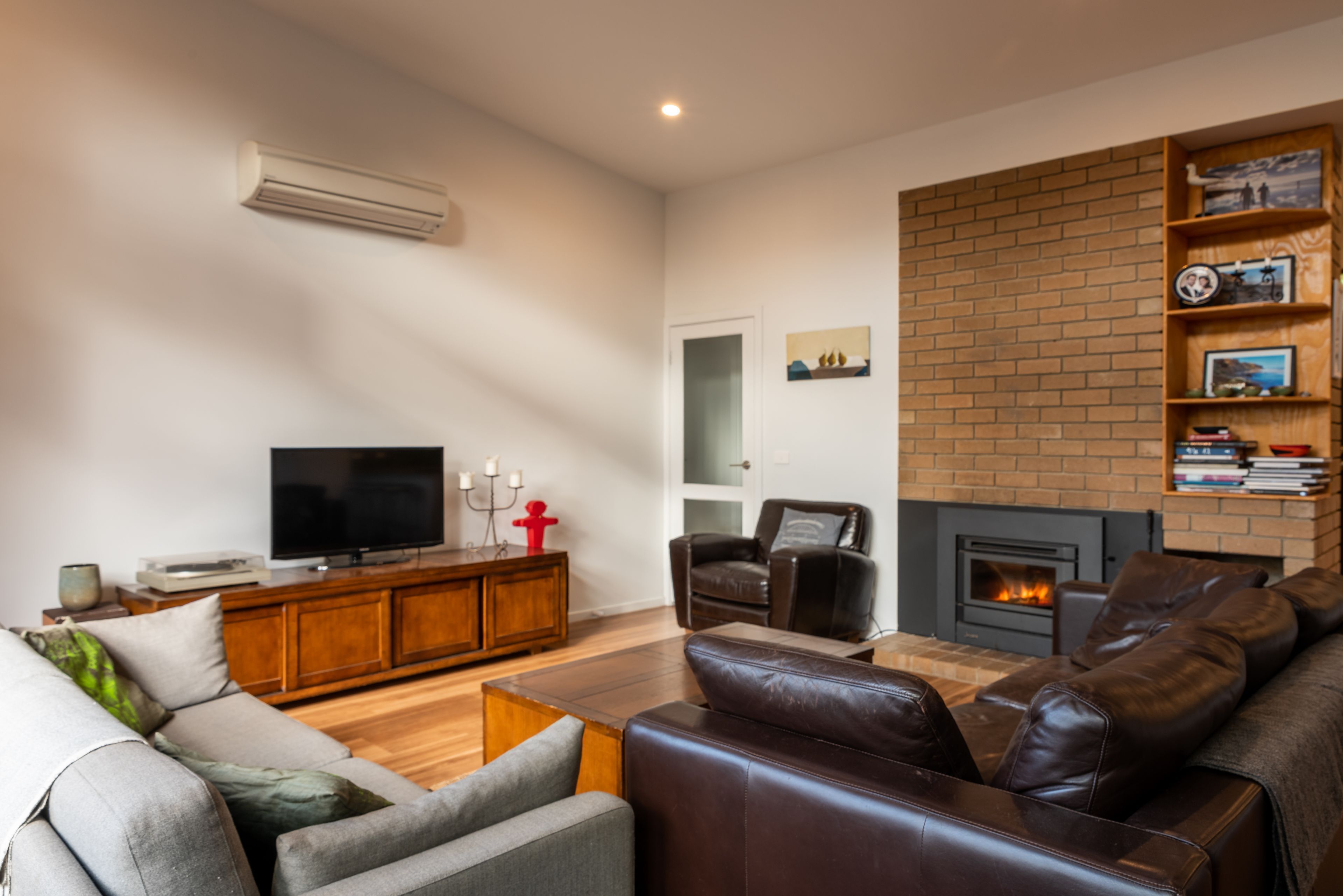 A living room with a fireplace, leather sofas, a TV, and a brick wall.