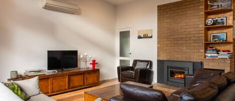 A living room with a fireplace, leather sofas, a TV, and a brick wall.