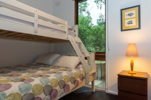 A bunk bed with a colorful quilt, a bedside lamp, and a window with a view of trees. - The Property (Anglesea)