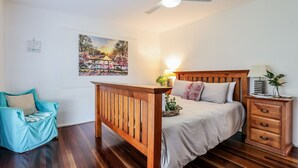 Ein Schlafzimmer mit einem hölzernen Bett, einem Nachttisch, einem Sessel und einem an der Wand befestigten Bild.