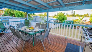 Eine überdachte Terrasse im Freien mit einem Esstisch, umgeben von Stühlen und einem Grill.