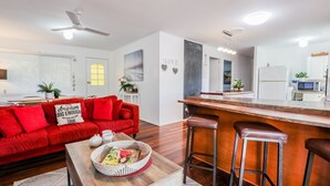 Ein modernes Wohnzimmer mit einem roten Sofa, einem Couchtisch und einer Küchenzeile mit Bar und Hockern.